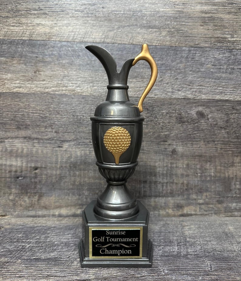 May include: A silver golf trophy with a gold golf ball design and a black base with a gold plaque that reads "Sunrise Golf Tournament Champion".