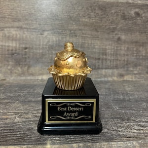 May include: Gold cupcake-shaped trophy with black base and the inscription "Best Dessert Award".