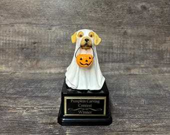 May include: A golden retriever dog dressed as a ghost holding a jack-o-lantern. The dog is on a black base with a gold plaque that reads "Pumpkin Carving Contest Winner".