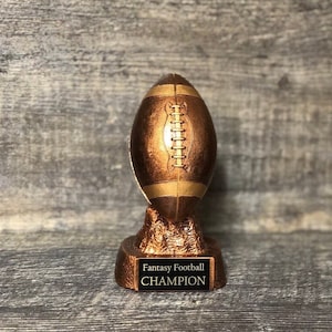 May include: A gold-colored football trophy with a black base. The base has the words "Fantasy Football CHAMPION" inscribed on it.