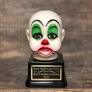 May include: A black and gold trophy with a white porcelain clown head. The trophy reads "Boyle Halloween Party Best Couples Costume 2022".