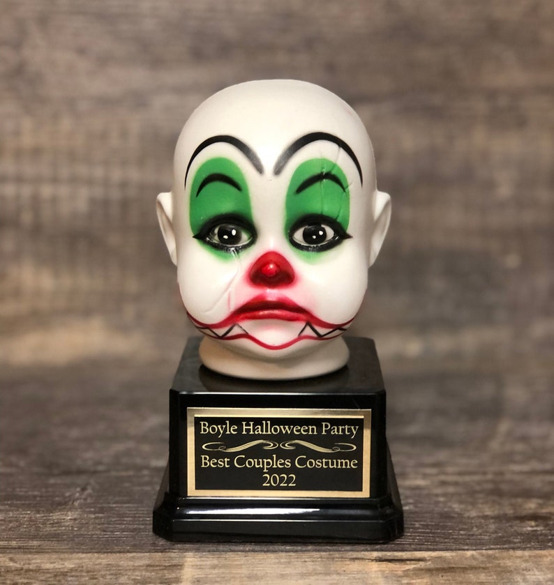 May include: A black and gold trophy with a white porcelain clown head. The trophy reads "Boyle Halloween Party Best Couples Costume 2022".