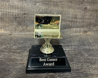 Könnte beinhalten: Eine goldene Laptop-Trophäe auf einem schwarzen Marmorsockel. Der Sockel trägt eine Plakette mit der Aufschrift "Best Gamer Award".
