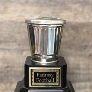 May include: A silver trash can trophy with a black base and a gold plaque that reads "Fantasy Football".