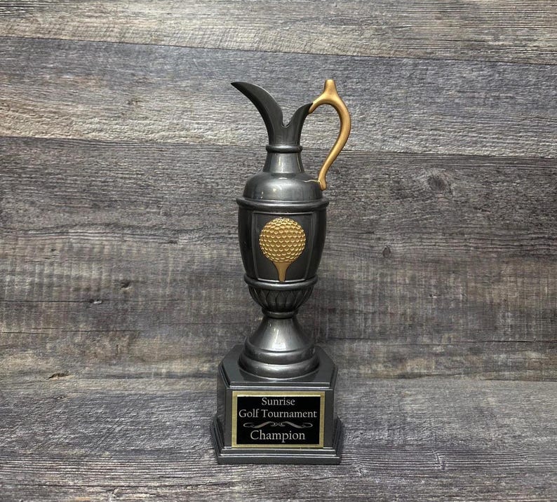 May include: A silver golf trophy with a gold handle and a gold golf ball design. The base of the trophy has a black plaque with the text "Sunrise Golf Tournament Champion".