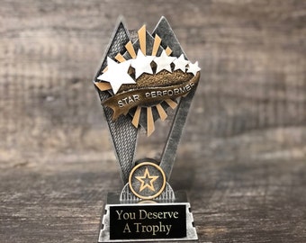 May include: A silver trophy with a black base that reads "You Deserve A Trophy." The trophy features a star design with the words "STAR PERFORMER" on a banner. The trophy has a star emblem.