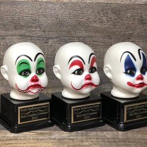 May include: Three black and gold award bases with white clown head figurines. The bases have gold plaques with the text "Boyle Halloween Party" and the categories "Best Couples Costume", "Best Girl Costume", and "Best Boy Costume".