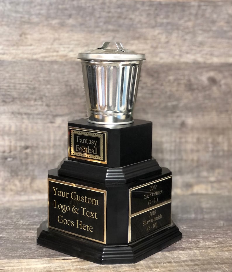 May include: A black trophy with a silver trash can on top. The trophy has three tiers with gold lettering. The top tier says "Fantasy Football". The middle tier says "Your Custom Logo & Text Goes Here". The bottom tier has the text "2019 Zach Grimes (2-11)" and "2018 Shawn Smith (3-10)".