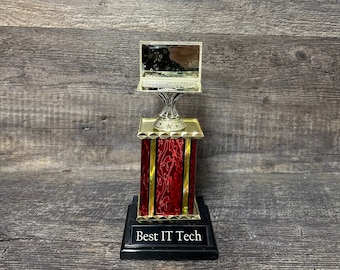 Könnte beinhalten: Eine goldfarbene Trophäe mit einem roten und goldenen Sockel. Die Trophäe zeigt einen silbernen Laptop obenauf. Der Sockel trägt die Aufschrift "Best IT Tech" auf einer schwarzen Plakette.