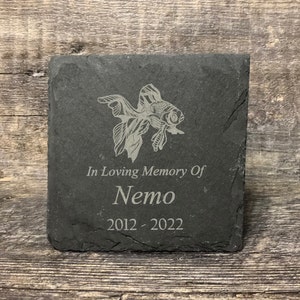 May include: Black slate memorial stone with a goldfish design, the text "In Loving Memory Of Nemo 2012 - 2022" is engraved on the stone.