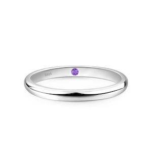 May include: A silver ring with a small, round, purple gemstone. The ring is smooth and polished, with a simple band design. The ring is likely made of sterling silver, as indicated by the "S925" marking. This ring is a piece of jewelry.