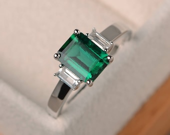 May include: A silver ring with a large emerald green gemstone and two smaller clear gemstones on the band.