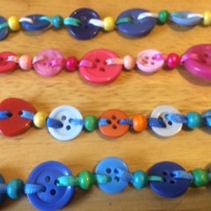 May include: Four colourful button necklaces with different coloured beads and buttons. The necklaces are made with a variety of colours, including blue, red, pink, yellow, and green.