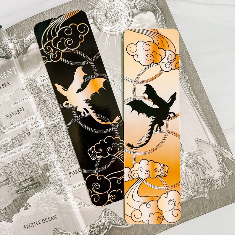 May include: Two dragon-themed bookmarks. One is black with a gold dragon and cloud design, the other is orange with a black dragon and cloud design. Both have a chain-like border and are set against a map.