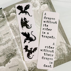 May include: Two white bookmarks with black dragon silhouettes and text. One bookmark features four dragon designs. The other bookmark has the text: "A dragon without its rider is a tragedy. A rider without their dragon is dead."
