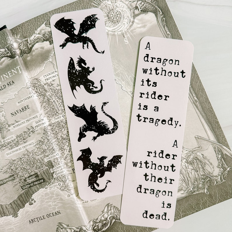 May include: Two white bookmarks with black dragon silhouettes and text. One bookmark features four dragon designs. The other bookmark has the text: "A dragon without its rider is a tragedy. A rider without their dragon is dead."