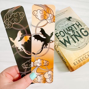 May include: Two dragon-themed bookmarks with gold accents and a book titled "Fourth Wing" by Rebecca. One bookmark is black with a gold dragon and cloud design. The other is orange with a black dragon and cloud design. The book has a circular design.