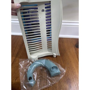May include: A beige plastic media storage rack featuring horizontal slots for organizing discs, accompanied by a separate, curved, light blue plastic base component that is enclosed in a clear plastic bag for protection and storage.