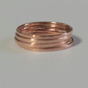 May include: A stack of five copper-colored rings. The rings are smooth and have a slight shine, reflecting the light. The rings are stacked on top of each other, creating a layered effect. The rings are likely jewelry.