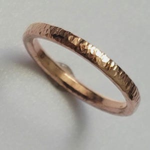 May include: A rose gold ring with a hammered texture. The ring has a thin band and a textured surface, reflecting light. The ring is a piece of jewelry.