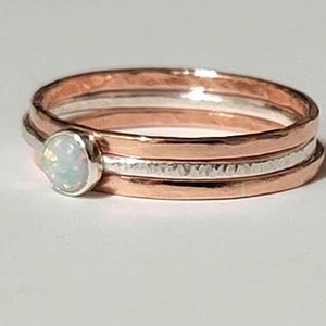 May include: A set of three rings, one silver and two rose gold, with a white opal gemstone. The rings are hammered and have a textured finish.
