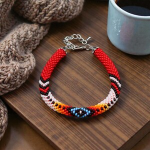 May include: A beaded bracelet featuring a tubular design with a vibrant pattern of red, black, white, orange, and light blue glass beads. The bracelet includes a silver-toned metal lobster claw clasp and an adjustable chain link extension.