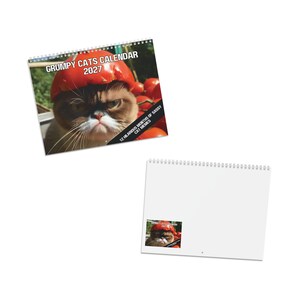 May include: A 2027 wall calendar featuring a cat wearing a red tomato as a hat on the cover. The text reads GRUMPY CATS CALENDAR 2027 and 12 HILARIOUS MONTHS OF SASSY CAT MEMES. The calendar is spiral-bound at the top with a white back page.