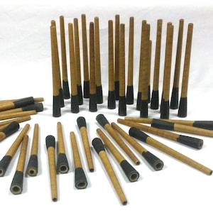 Peut inclure: Une collection de chevilles en bois avec des embouts peints en noir. Les chevilles sont disposées en cercle et en demi-cercle sur une surface blanche.