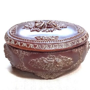 Peut inclure: Une boîte à bijoux ovale en bois brun avec des motifs floraux et des cœurs complexes. La boîte a un couvercle à charnière et une base détaillée.