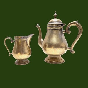 Peut inclure: Un ensemble vintage de théière et de crémier en argent. La théière a un corps arrondi avec une poignée et un bec décoratifs. Le crémier a une forme similaire avec un bec plus petit.