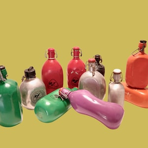Pode incluir: Uma coleção de onze cantis de metal em várias cores, incluindo verde, vermelho, prateado, laranja e roxo. Cada cantil possui um mecanismo de fecho com alavanca de arame e um pequeno logótipo circular impresso na frente de várias unidades.