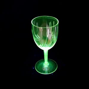 May include: A glowing neon green glass goblet featuring a delicate etched pattern of thin, curved lines along the bowl. The stem and circular base are also made of the same vibrant, translucent green glass, creating a uniform appearance.