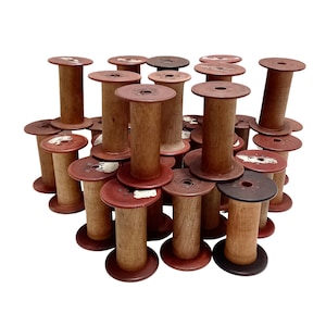 May include: A collection of vintage wooden spools in various shades of brown and red. The spools have a cylindrical shape with a flat top and bottom, and a hole in the center. Some spools have remnants of paper labels.