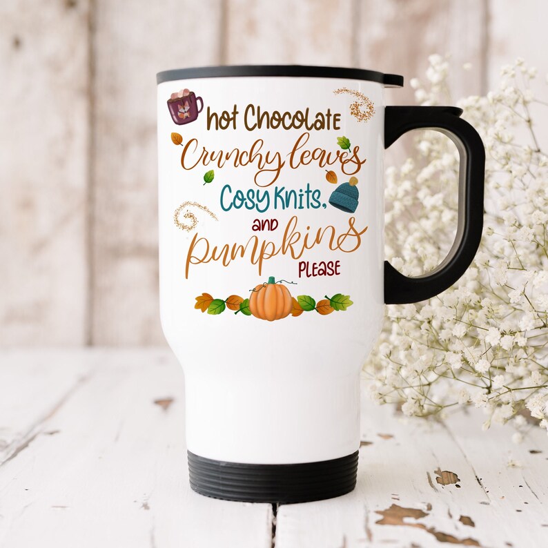 Puede incluir: Taza de viaje blanca con asa y tapa negras. La taza tiene un dise&ntilde;o de oto&ntilde;o con el texto "hot Chocolate Crunchy leaves Cosy Knits. and pumpkins PLEASE".
