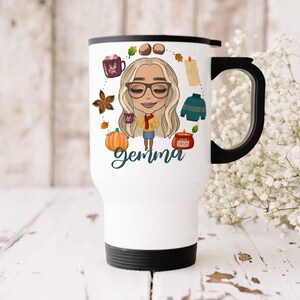 Puede incluir: Taza de viaje blanca con tapa y asa negras. La taza presenta una ilustraci&oacute;n de dibujos animados de una mujer con cabello rubio y gafas, rodeada de iconos de tem&aacute;tica oto&ntilde;al como una calabaza, una vela y un su&eacute;ter. El texto "gemma" est&aacute; escrito debajo de la ilustraci&oacute;n.