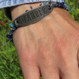 May include: A silver bracelet with blue beads and a metal charm that says "WANDER".