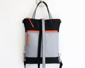 May include: A black and grey convertible backpack with orange zipper pulls. The bag has a top handle and adjustable shoulder straps.
