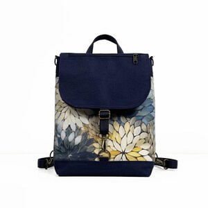May include: A navy blue canvas backpack with a floral pattern. The backpack has a flap with a buckle closure and a zippered pocket on the front.