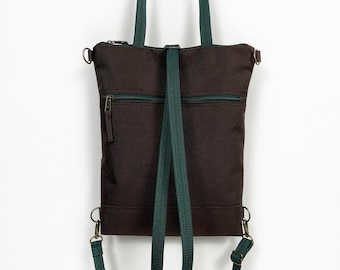 May include: A brown canvas tote bag with a green adjustable strap. The bag has two zipped pockets on the front and a zipped pocket on the back. The bag can be worn as a backpack or a shoulder bag.