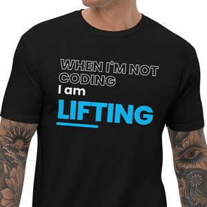 May include: Black t-shirt with the text "WHEN I'M NOT CODING I AM LIFTING" in white and blue. The shirt is short-sleeved and has a crew neck. The text is centered on the chest.