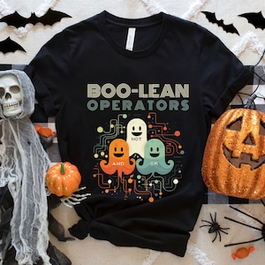 May include: Black t-shirt featuring the text "BOO-LEAN OPERATORS" and a graphic of three cartoon ghosts labelled "AND", "NOT", and "OR". Halloween decorations, including pumpkins, spiders, and bats, surround the shirt.