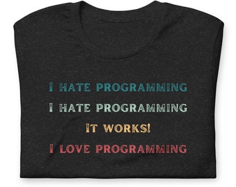May include: Dark gray t-shirt with the text "I HATE PROGRAMMING" in teal, "I HATE PROGRAMMING" in light teal, "IT WORKS!" in gold, and "I LOVE PROGRAMMING" in red. The shirt is folded.
