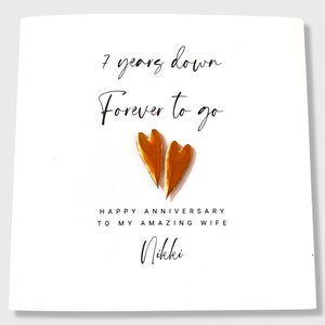 May include: A white greeting card featuring the black text 7 years down Forever to go, two metallic copper-colored heart shapes, and the black text HAPPY ANNIVERSARY TO MY AMAZING WIFE followed by the name Nikki in a script font.