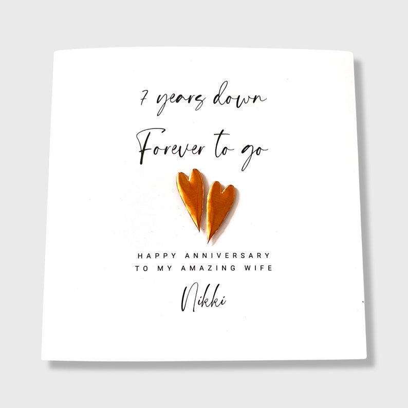 Personalised white 7th anniversary card with the text "7 years down, Forever to go." Two genuine copper hearts are below the text. The card also says Happy Anniversary to my amazing wife followed by the personalised name.