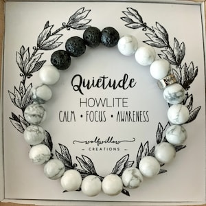 May include: A white and black beaded bracelet with the words "Quietude Howlite Calm Focus Awareness" and "wolfwillow creations" on a white card.