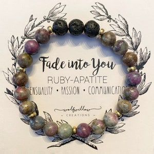 Könnte beinhalten: Ein Armband aus Rubin-Apatite und Lavasteinen. Das Armband ist goldfarben und hat den Text "Fade into You" und "Ruby-Apatite" auf einer Karte dahinter. Die Karte hat auch den Text "Sensualität, Leidenschaft, Kommunikation" und "wolfwillow creations".
