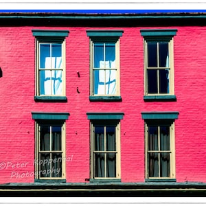 May include: A red brick building with six windows. The windows have white trim and are divided into three panes. The building has a dark green roof.
