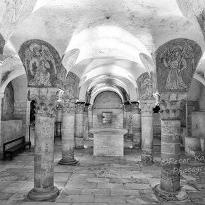 May include: Black and white photograph of a stone crypt with arched ceilings and columns. The crypt is decorated with painted figures of angels. The photo is taken from the centre of the crypt, looking towards the back wall.