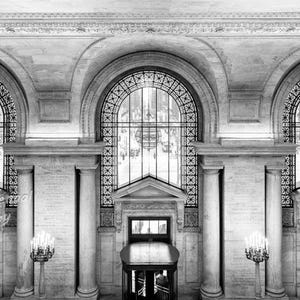 May include: Black and white photograph of a grand interior space with arched windows and ornate architectural details. The image features tall columns, decorative lighting, and multiple doorways, creating a sense of scale and historical significance.