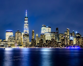 Pode incluir: Uma vista noturna do horizonte da cidade de Nova Iorque com a Freedom Tower iluminada no centro.
